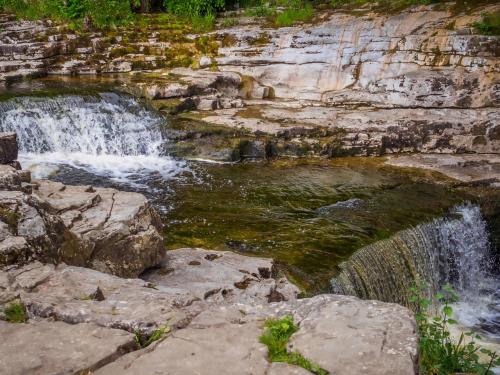 a waterfall on the side of a mountain with rocks at Winskill Cottage in Settle