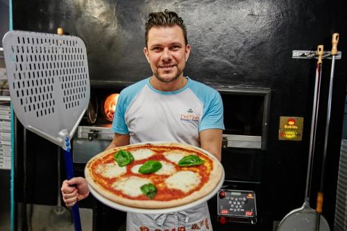 a man holding a large pizza with a spatula at Dei Fiori Camping Village in Cavallino-Treporti