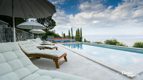 a swimming pool with lounge chairs and an umbrella at Apartments Vunić in Mošćenička Draga