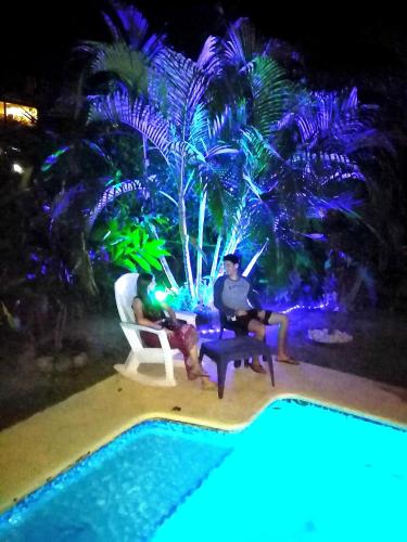 two men sitting on chairs next to a pool at night at The Blue House Panama in Chame