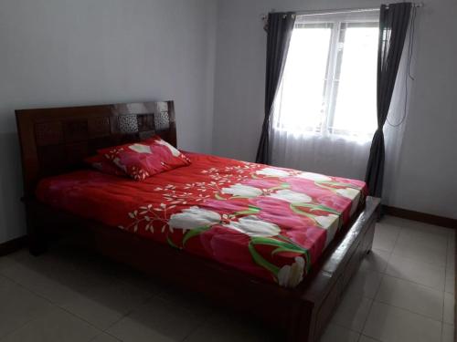 a bedroom with a bed with a red comforter and a window at Homestay Ayuning Kuningan in Jalaksana