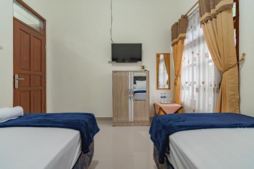 1 dormitorio con 2 camas y TV. en The Lima Guest House Syariah Mitra RedDoorz, en Cirebon