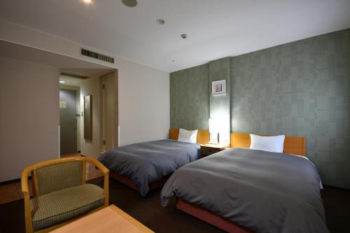 een hotelkamer met 2 bedden en een stoel bij Bell's Inn Tsuchiura in Tsuchiura