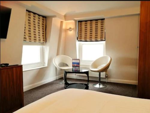 a bedroom with two chairs and a table and two windows at Legends Hotel in Brighton & Hove