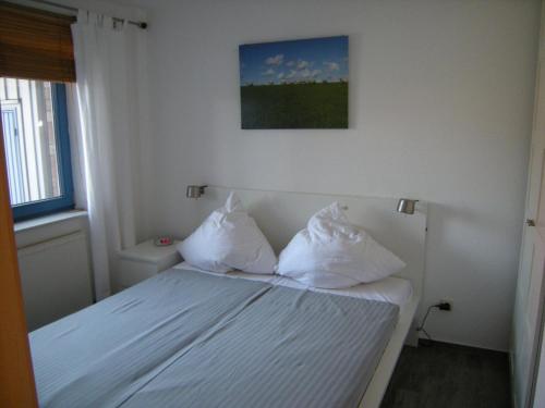 Schlafzimmer mit einem Bett mit weißer Bettwäsche und Kissen in der Unterkunft Strandlicht in Horumersiel