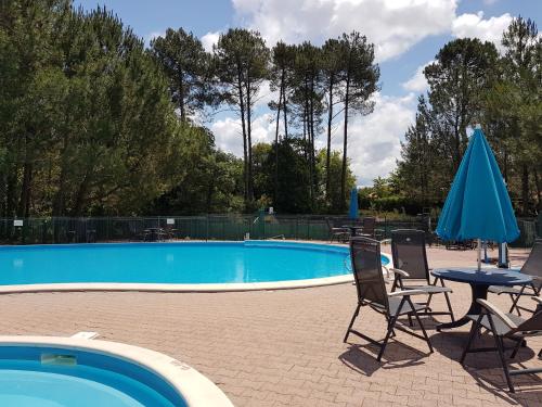 - une piscine avec 2 chaises, une table et un parasol bleu dans l'établissement Village Océlandes, à Saint-Julien-en-Born