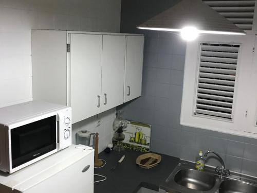 a kitchen with white cabinets and a sink and a microwave at Le Belleplaine in Le Gosier