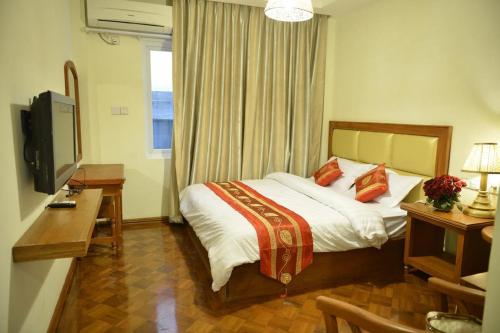 a bedroom with a bed and a desk and a television at Gold Yadanar Hotel in Mandalay