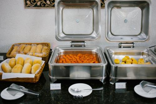a buffet with trays of food on a counter at VOA Express Inn Hotel Orquídea in Várzea Paulista