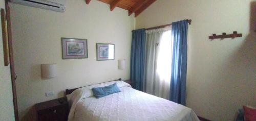 een slaapkamer met een bed en een raam met blauwe gordijnen bij Lo de la Omi in Villa General Belgrano
