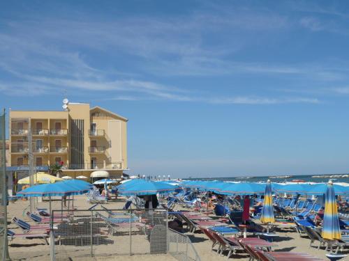 a beach with many chairs and blue umbrellas at Hotel Primavera sul mare in Lido di Savio