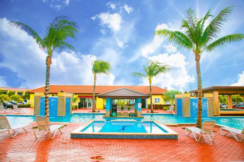 a swimming pool with palm trees and a house at Pearl Aruba Condos in Palm-Eagle Beach