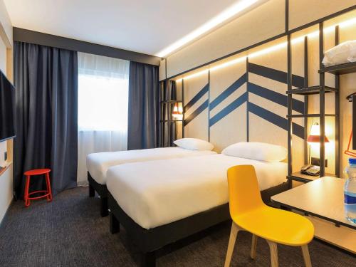 a hotel room with two beds and a yellow chair at ibis Styles Geneve Palexpo Aeroport in Geneva