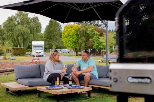 a man and woman sitting on a couch under an umbrella at Hanmer Springs TOP 10 Holiday Park in Hanmer Springs