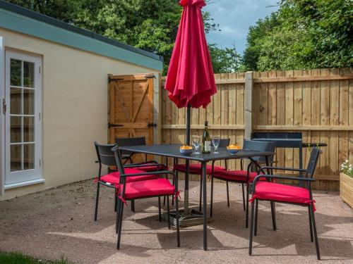 een zwarte tafel met rode stoelen en een paraplu bij Vicarage Cottage in Kenton