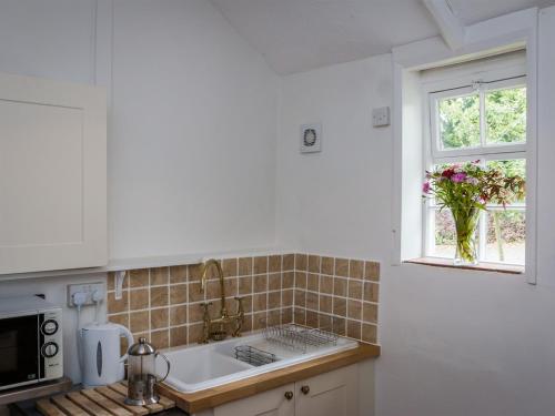 a white kitchen with a sink and a window at Vicarage Cottage in Kenton
