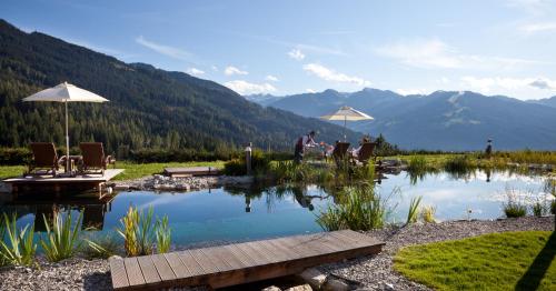 a man standing in front of a pond with chairs and umbrellas at Naturhotel Edelweiss Wagrain in Wagrain