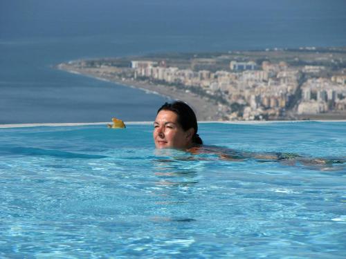 a woman in a swimming pool with a city in the background at Villa Perla Blanca in Sayalonga