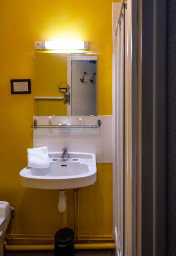 a yellow bathroom with a sink and a mirror at Hotel Auberge des Remparts in Laval