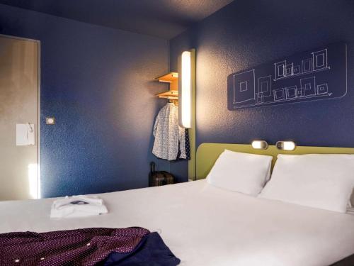 - une chambre avec un lit blanc et un mur bleu dans l'établissement ibis budget Arles Sud Fourchon, à Arles