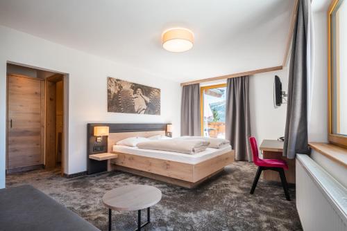 a bedroom with a bed and a red chair at Ursprung Panorama Hotel Königsleiten in Königsleiten