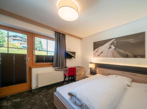 a bedroom with a bed and a desk and a window at Ursprung Panorama Hotel Königsleiten in Königsleiten