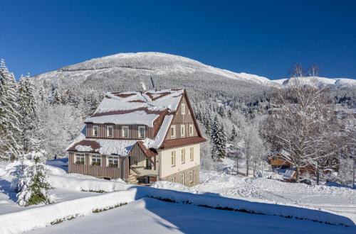a house covered in snow in front of a mountain at MINERVA in Špindlerův Mlýn