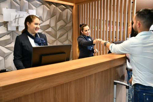 Um homem a apertar a mão a uma mulher atrás de uma secretária. em Holiday Inn Express Asuncion Aviadores , an IHG Hotel em Assunção