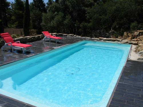 a swimming pool with two red chairs at Les Romarins in Aigne