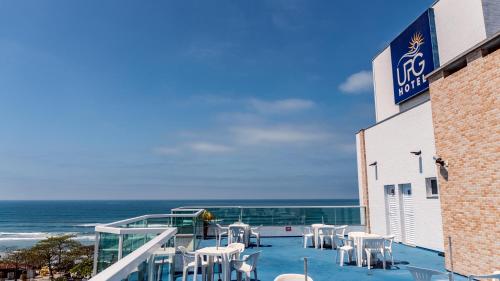 a balcony with white tables and chairs and the ocean at UPG Hotel in Ubatuba