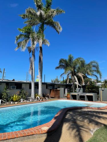 a swimming pool with palm trees in the background at Queens Beach Hotel in Bowen