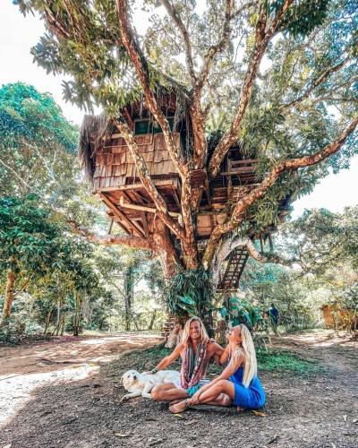 two women and a dog sitting in front of a tree house at Art Jungle Eco Lodge in Itacaré