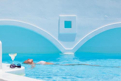 a person in a swimming pool with a drink and glasses at On The Rocks - Small Luxury Hotels of the World in Imerovigli