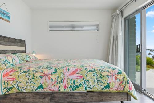 um quarto com uma cama com colcha floral e uma janela em Soleil on Omana - Omana Beach Holiday Home em Maraetai