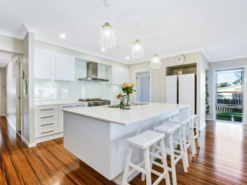 a white kitchen with a large white counter and stools at Sun Daze at Smithies in Smiths Lake