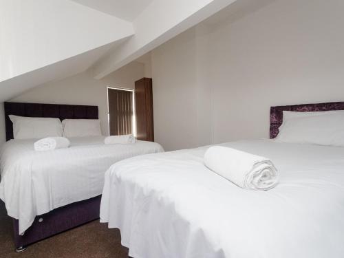two beds in a bedroom with white sheets at Eastpark Residence in Leeds