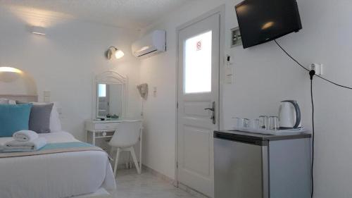 a white bedroom with a bed and a television on the wall at Kafieris View in Firostefani
