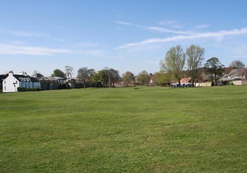 a large green field with houses in the background at Sylvan Orchard in Gullane