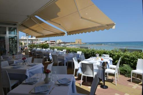 a restaurant with white tables and chairs and the ocean at Hotel Mirage in Torre Santa Sabina