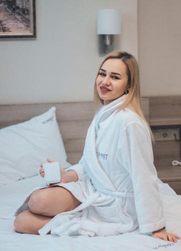 a woman sitting on a bed holding a cell phone at Arena Summit Apart Hotel in Kyiv