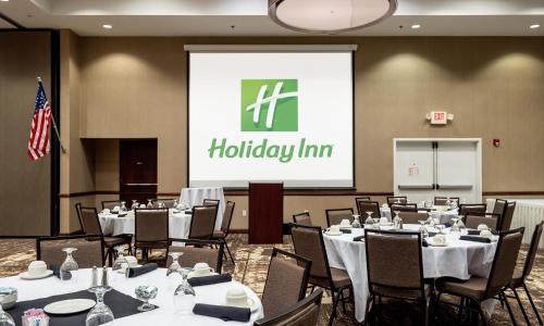 a conference room with tables and chairs and a screen at Holiday Inn Conference Center Marshfield by IHG in Marshfield