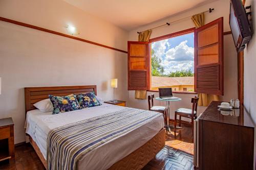 a bedroom with a bed and a desk and a window at Hotel Nacional Inn Araxá Previdência in Araxá
