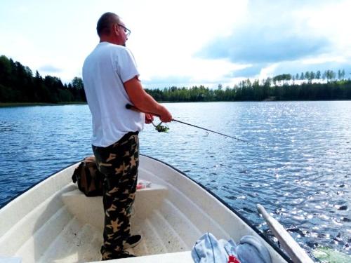 un homme debout dans un bateau tenant un canne de pêche dans l'établissement Lila Stuga, à Väja