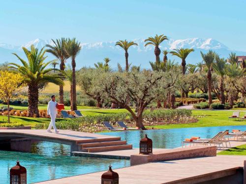 Fairmont Royal Palm Marrakech في مراكش: رجل يمشي على ممشى بجانب بحيرة