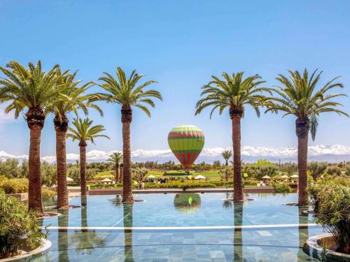 マラケシュにあるFairmont Royal Palm Marrakechのヤシの木が植えられたプール上空を飛ぶ熱気球