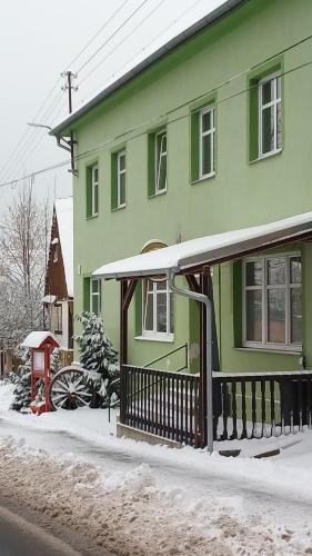 a green house with a porch in the snow at Ubytovaní Šaslun in Kolešov