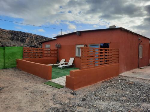 une maison rouge avec une terrasse et deux chaises dans l'établissement Casa rural, Naturaleza, Relax, Vacaciones, à Teguitar