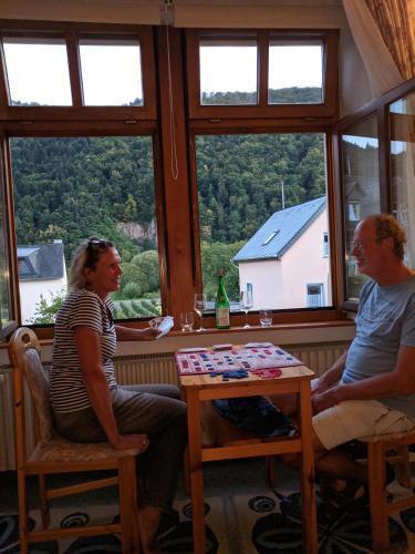 mężczyzna i kobieta siedzący przy stole patrzący przez okno w obiekcie Weingut Pension Hammes-Krüger w mieście Ellenz-Poltersdorf