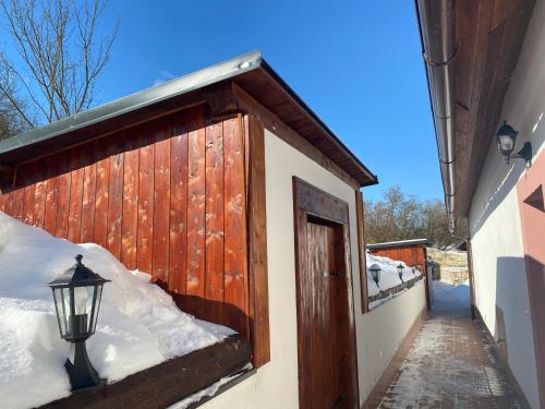 a building with a wooden door and snow on the ground at SG chalupa ŠTIKOV - Podkrkonoší - s celoročním privátním wellness in Nová Paka