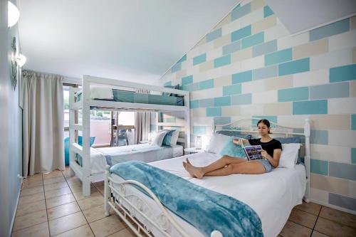 a woman sitting on a bed reading a book at Heart of Airlie Beach Apartment in Airlie Beach